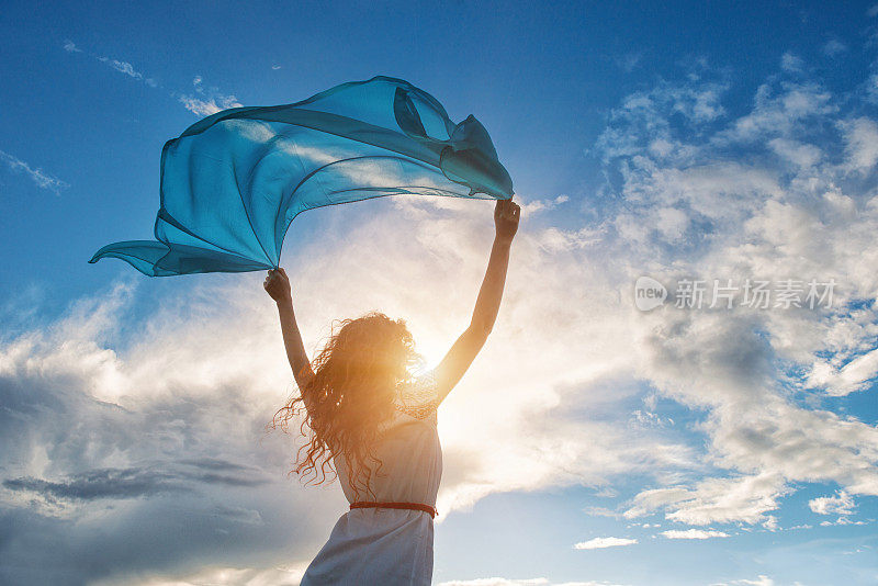 美丽的年轻女子拿着蓝色的围巾在风中