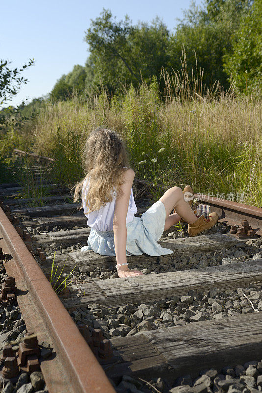 穿着皮靴的少女坐在生锈的铁轨上