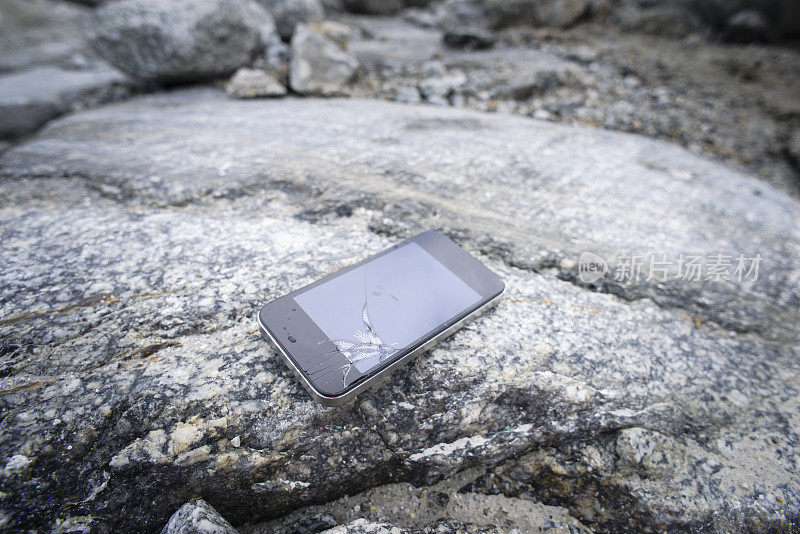 屏幕破碎的智能手机躺在户外的岩石上
