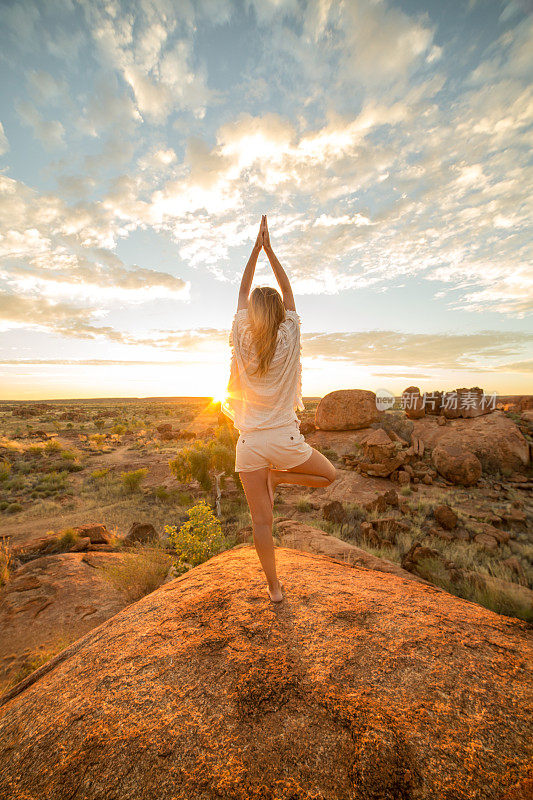 日出时，女性在巨石上练习瑜伽