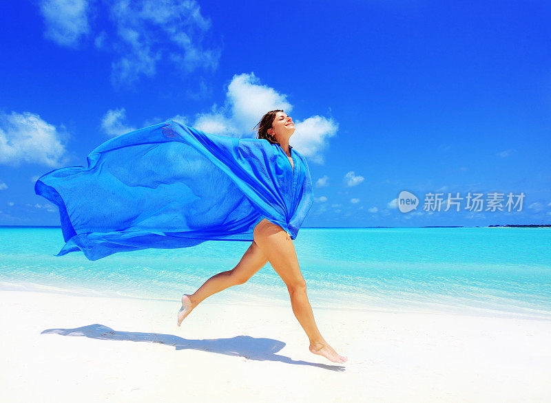 穿着长纱笼在海滩上跑步的快乐女人。