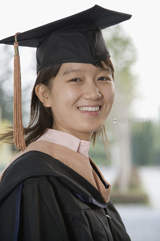 年轻女子在毕业礼服微笑，特写，肖像