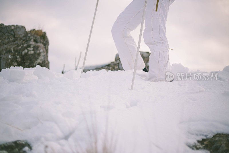 近景美丽的年轻女子在冬天的衣服站在一边，手拿木棍的背景雪山