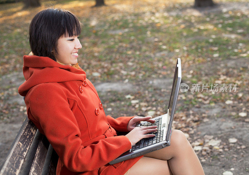 一个年轻的亚洲女孩在公园里用笔记本电脑打字。