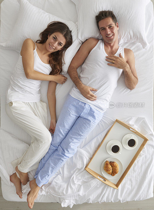 一对夫妇躺在床上，端着早餐盘