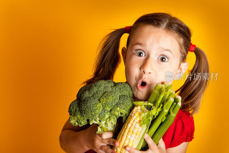 兴奋的小女孩拿着西兰花，玉米，芹菜