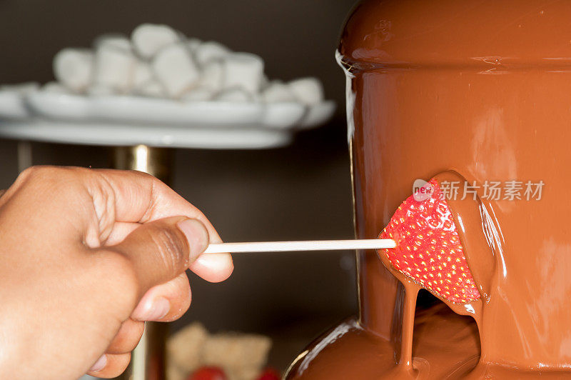 把草莓浸在巧克力瀑布里。