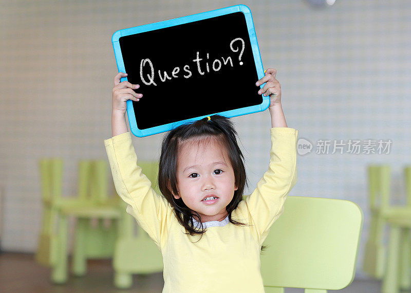 可爱的小女孩拿着写有“问题?”在孩子的房间里。教育的概念。