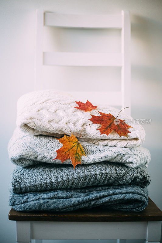 一堆暖和的衣服和秋叶放在椅子上。旅游的概念