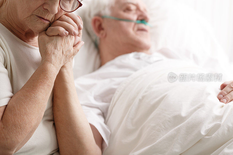 老人躺在病床上，他的妻子牵着他的手