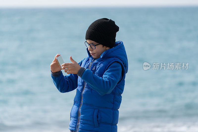 快乐男孩在海滩上散步，用手机自拍