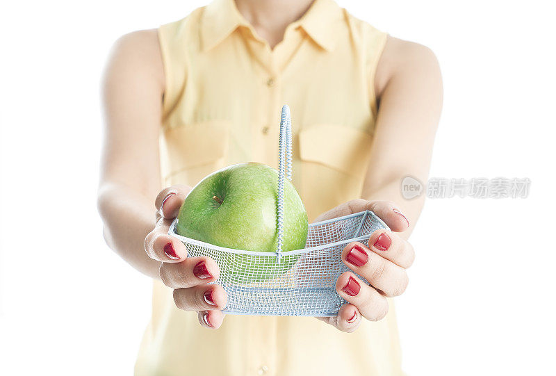 一个女人拿着一个装在迷你购物篮里的绿苹果