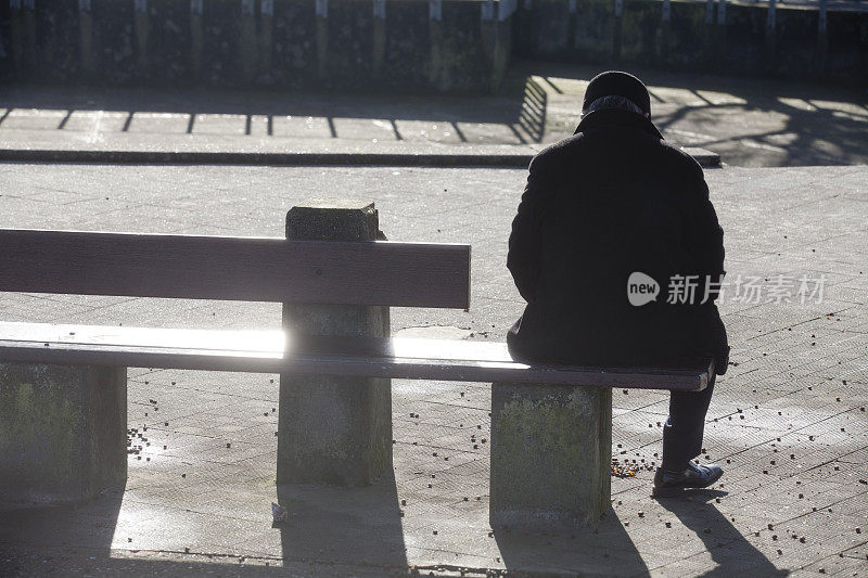 一个孤独的人坐在阳光下的长椅上
