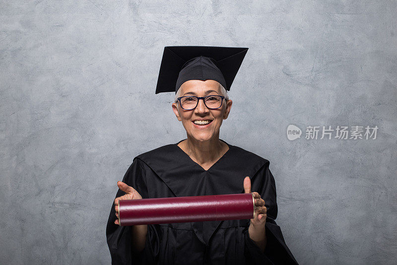 快乐的老女人穿着毕业礼服，戴着眼镜，拿着文凭