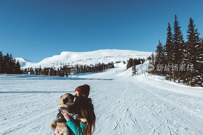 女人和狗在山上滑雪胜地的雪上玩