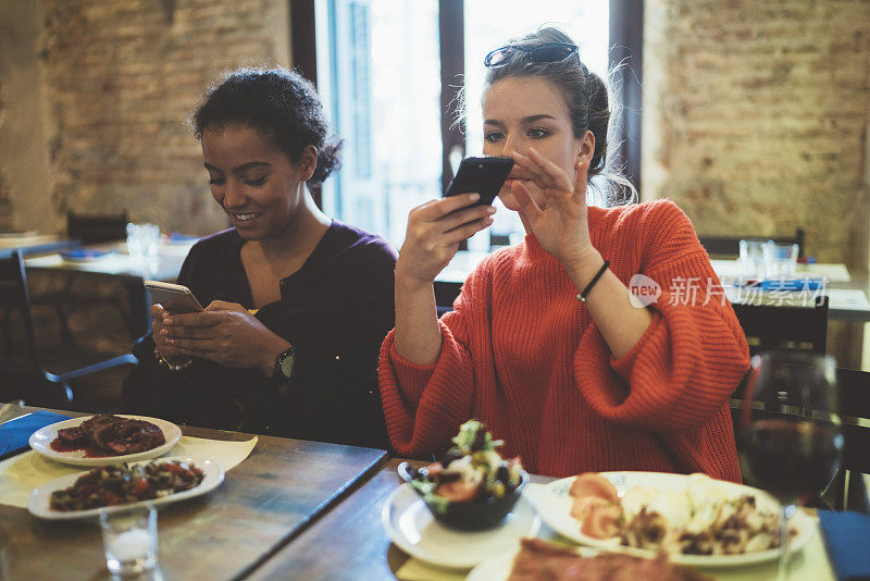 两个女人在餐馆里给食物拍照