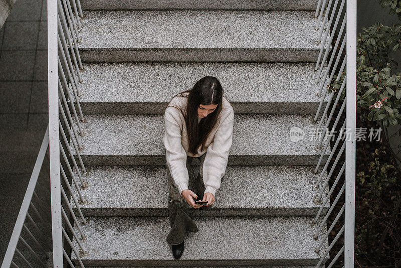 年轻女子拿着智能手机坐在楼梯上