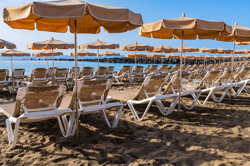 西班牙特内里费岛的洛斯克里斯蒂亚诺斯湾海滩，配有日光浴床和雨伞