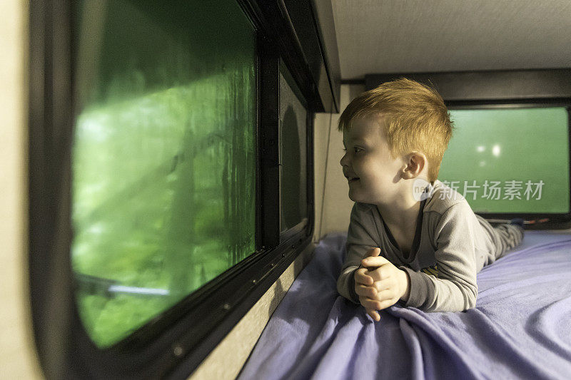 雨中的小红发男孩在野营拖车里望着窗外