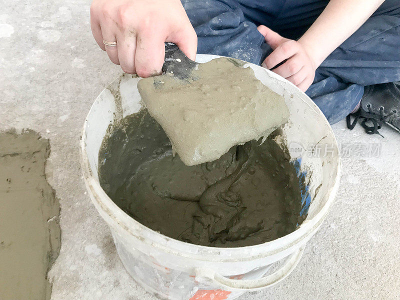 建筑工手用金属刮刀在一个大的白色塑料建筑桶中揉捏灰泥、瓷砖胶水、用于修复公寓、房屋的水泥、找平墙壁和浇筑平整面