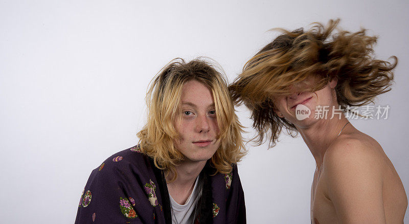 年轻的男音乐家随着音乐的节拍甩动头发，而他的朋友却在看镜头。