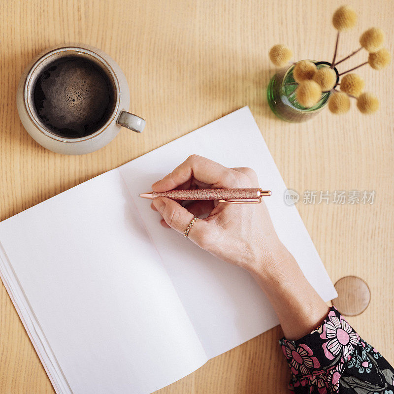女人在笔记本的空白页上写字，喝着咖啡