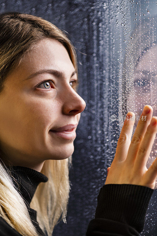 体贴的年轻女子看透过窗户与雨滴