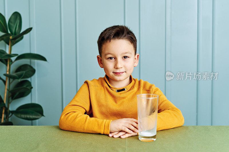 6-7岁可爱的孩子在桌上喝牛奶。他知道他需要喝牛奶来保持骨骼健康。他喜欢牛奶。