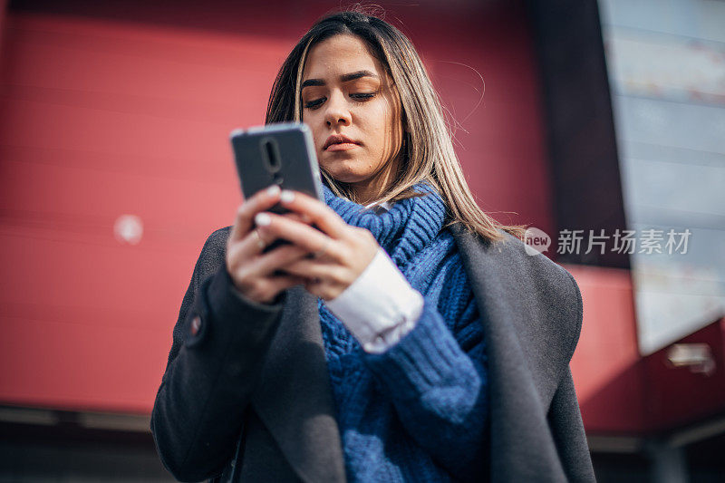 美丽的年轻女子站在购物中心前面，并使用智能手机