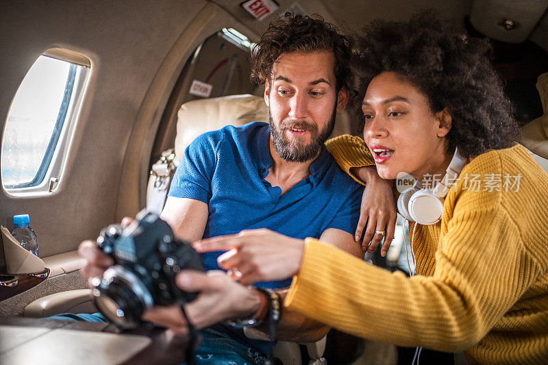 在一架私人飞机上，一名著名的年轻女子指着她的伴侣对着一台单反相机
