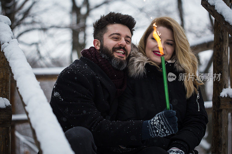 夫妇拿着烟花。一对年轻夫妇在冬天的森林里拿着火花。快乐微笑的夫妇与节日烟花庆祝圣诞户外