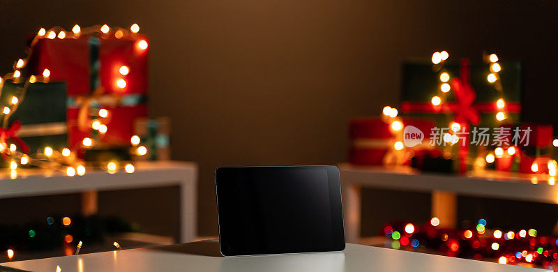 白色桌子上的数码平板，散焦圣诞灯和背景礼物，散焦