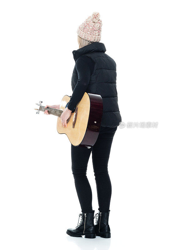 白人女吉他手站在白色的背景，穿着暖和的衣服，拿着原声吉他