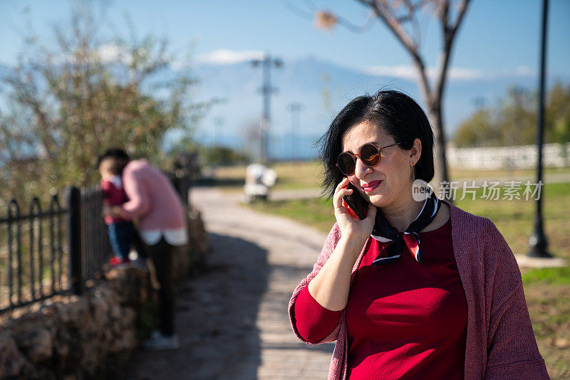 一位成年妇女在打电话，而祖母在室外照顾婴儿孙女