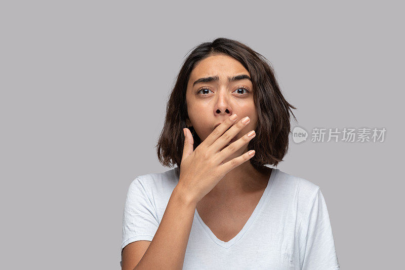 年轻女子越过孤立的背景打哈欠疲倦用手捂住嘴。