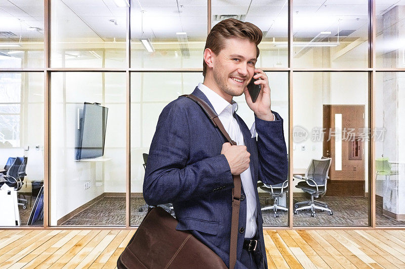年轻的男性专家站在会议室里，背着肩包，拿着包，拿着手机
