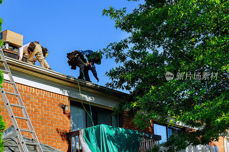 一名屋顶工人用气枪钉住瓦片，取代屋顶保护层