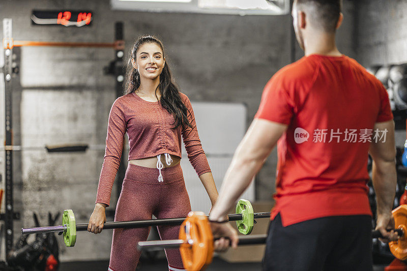 年轻健康的夫妇穿着运动服，在健身房进行举重训练