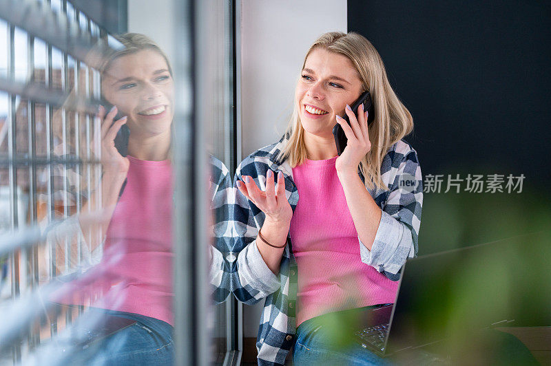 年轻女子坐在窗边，手提电脑和手机