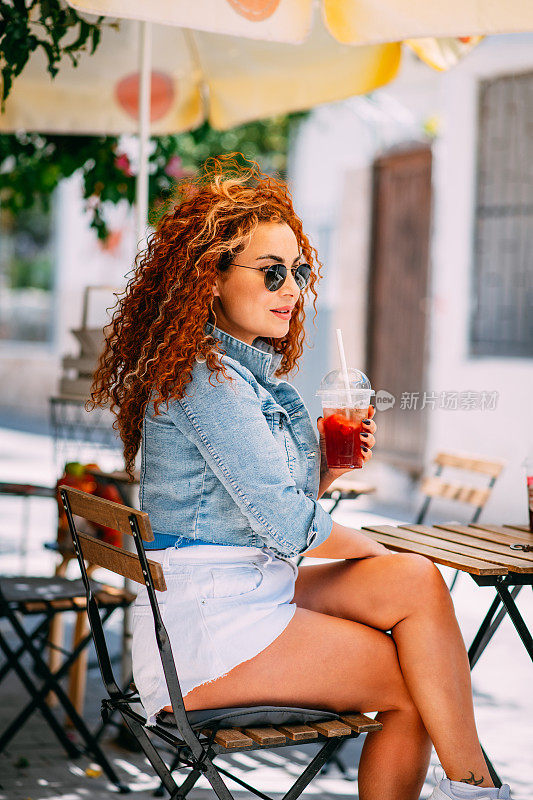在阳光明媚的天气里，女人在户外咖啡馆喝清爽的冷冻咖啡