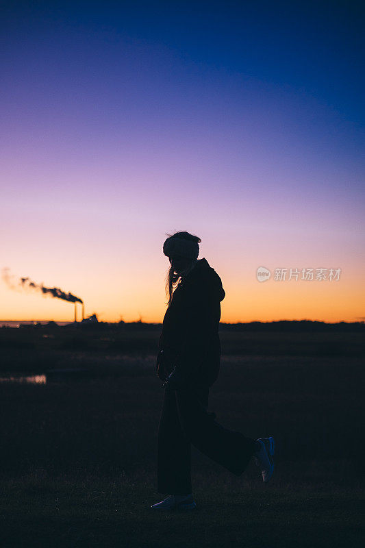 一名妇女在夕阳下走过煤油混合发电厂