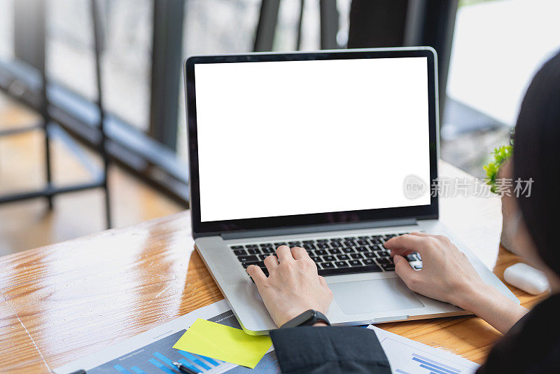 一个女商人在办公室用笔记本电脑的空白屏幕工作的特写。模拟。