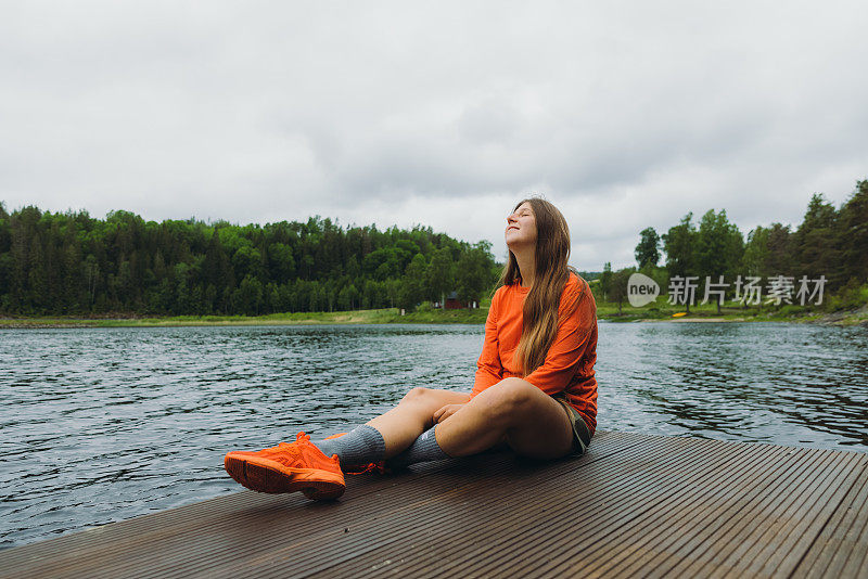 年轻女子坐在码头上，凝视着夏日的瑞典湖边