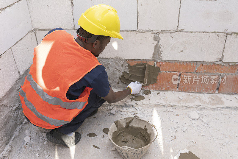 非裔美国建筑工人在建筑工地用泥铲在墙上抹砂浆