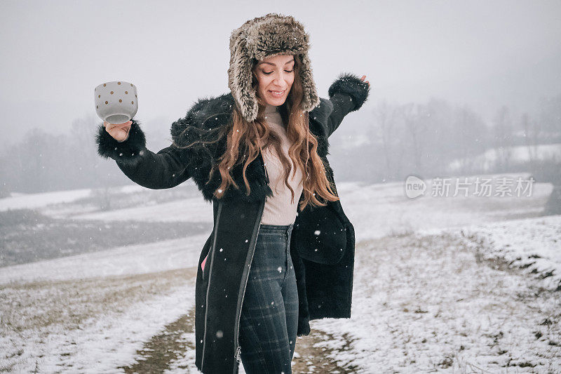 站在雪地上拿着一杯茶的年轻女子