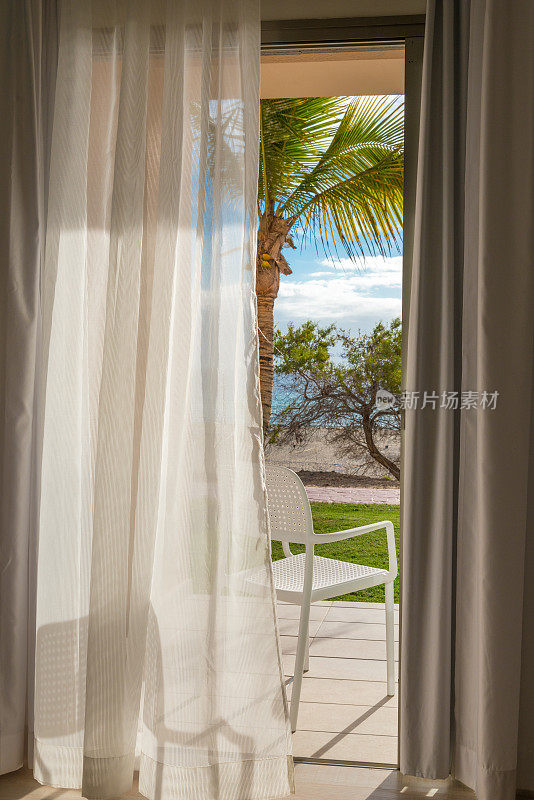 窗帘在风中与棕榈树和海滩的视野