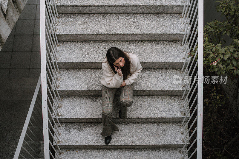 年轻女子拿着智能手机坐在楼梯上