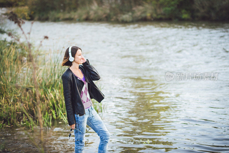 年轻的白人妇女戴着耳机享受在河边。