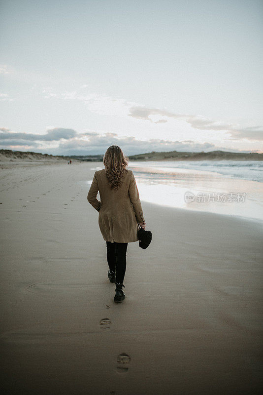 一个年轻女子在冬天的夕阳下走过海滩