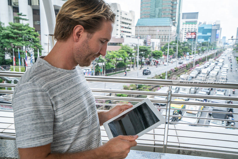 年轻白人男性在曼谷城市使用数字平板电脑户外-人们旅行的概念。一个人在户外使用科技工作